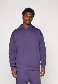 Paarse capuchontrui gemaakt van zacht materiaal. Heeft een losse pasvorm, geribbelde manchetten en een geperst logo op de borst.