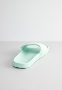 Sandale à glissière vert menthe avec une large bride supérieure, semelle intérieure texturée et semelle plate, ornée de accents blancs le long de la bride.