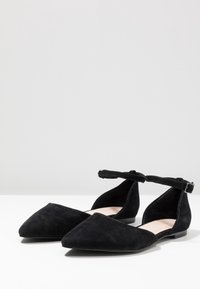 Ballerines en daim noir avec bout pointu, bride à la cheville et talon bas. Présentent un design découpé sur les côtés et une doublure intérieure lisse.