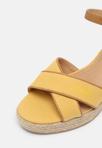Yellow canvas espadrille sandal with crossed straps, tan leather accent, and woven jute sole. Features embroidered logo detail.