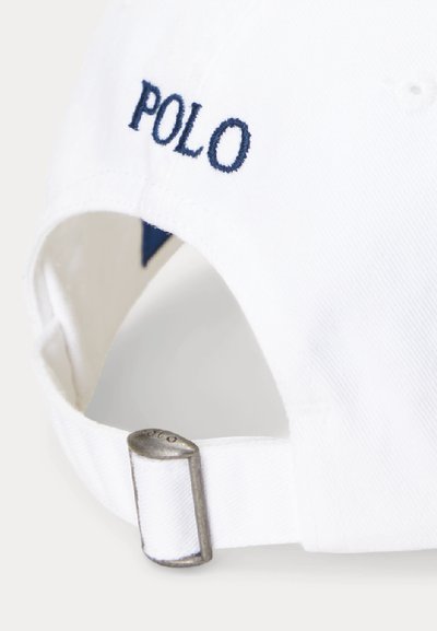 Bílý bavlněný pásek s kovovou přezkou rytou "POLO" a tmavě modrým vyšitým textem "POLO" blízko přezky.