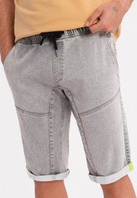 Pantalones cortos de mezclilla gris con cintura con cordón, bolsillos laterales, dobladillos enrollados y acentos en verde neón. Presenta detalles de costura visibles y un ajuste relajado.