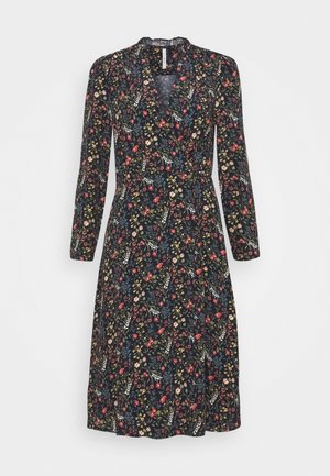 Kukkakuvioinen mekko, jossa on pitkät hihat, syvä V-aukko ja vyötäröä korostava leikkaus. Tummalla pohjalla värikkäitä kukkia ja lehtiä, pituus puoliväliin pohjetta.