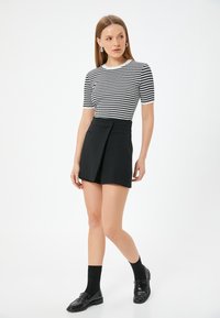 Sorte plissee shorts med to foran lommer, iført en stribet striktrøje i sort og hvid samt sorte strømper sammen med skinnende loafers.
