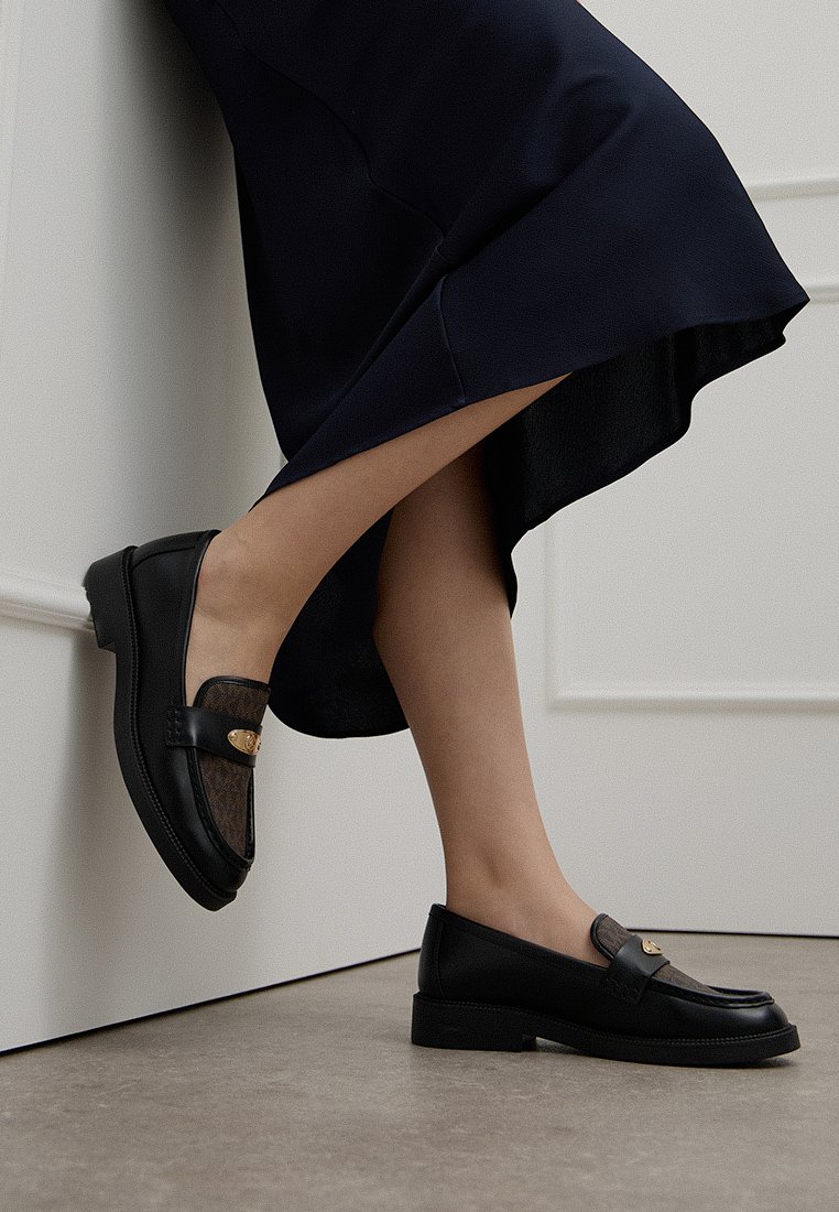 Zwarte leren loafers met een gestructureerd detail en gouden hardware. Laag profiel met een ronde neus en een platte rubberen zool.