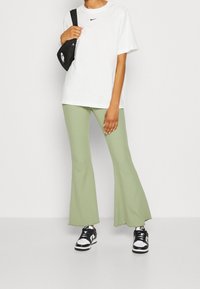 Vit bomullst-shirt med svart Nike-logotyp, kombinerad med ljusgröna ribbade utsvängda byxor och svartvita sneakers. Svart axelväska.