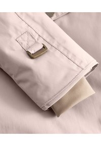Lichtroze waterdichte jas met een beige binnenmanchet; heeft een metalen gesp en gestikte accenten voor duurzaamheid.