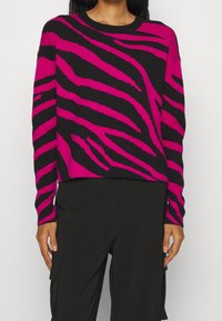 Maglione a maglia a righe zebrato magenta e nero con colletto a girocollo e maniche lunghe, abbinato a pantaloni cargo neri. Texture morbida.
