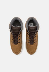 Brązowe zamszowe sneakersy z szarym materiałowym wykończeniem, okrągły czubek, sznurowany fason i wyściełana podeszwa. Posiadają naszywkę z logo na języku.