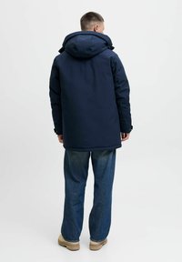 Marineblå parka jakke med hætte, der har en afslappet pasform, lange ærmer og en glat overflade. Styling med lyseblå brede jeans.