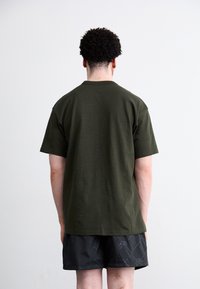 Oliven grøn kortærmet t-shirt med en simpel crew neck, lavet af blødt stof, parret med sorte mønstrede shorts med et logo.