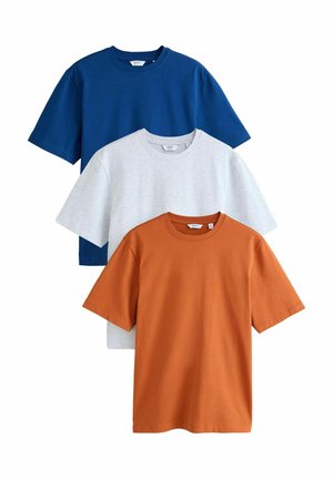Trois t-shirts unis à manches courtes et col rond en orange brûlé, gris clair et bleu marine, disposés en chevauchement sur un fond blanc.