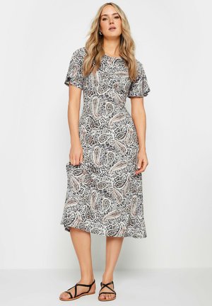 Robe à motifs paisley noir et blanc avec des manches courtes, un col rond et une jupe évasée. Portée avec des sandales plates noires.