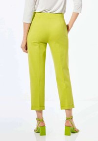 Limegrüne, maßgeschneiderte Hose mit hoher Taille, geradem Bein und umgekrempelten Säumen, kombiniert mit grünen Sandalen mit Blockabsatz und Riemchen.