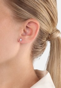 Örhängen med stenar i klar färg, satta i en enkel metallfäste. Designen har en rund form med en polerad yta.