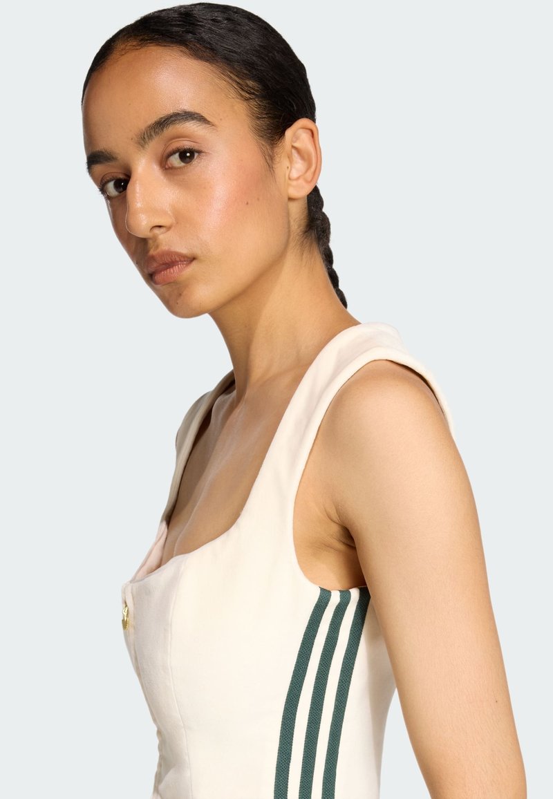 Lichtbeige jurk met een vierkante halslijn, schouderbanden en groene verticale strepen aan de zijkant. Bevat een gouden knoopdetail.