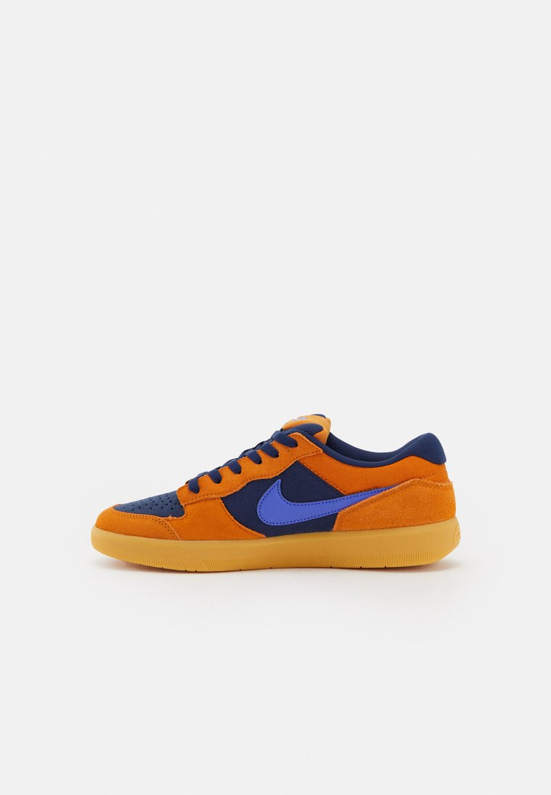 Basket de suède orange et en maille marine avec un swoosh Nike bleu, zone de orteil texturée et semelle en caoutchouc d'une teinte jaunâtre.