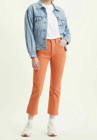 Veste en jean bleu clair, t-shirt blanc et jean droit orange. Completé par des baskets blanches et des chaussettes montantes.