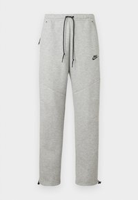 Sive Nike trenirke s pojasom na vezanje, bočnim džepovima i elastičnim manžetama. Imaju glatku teksturu i kontrastni crni detalj s logotipom.