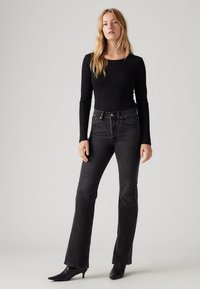 Haut noir à manches longues associé à un jean flare taille haute en denim foncé et des escarpins noirs à bout pointu. Tissu lisse avec un minimum de détails.
