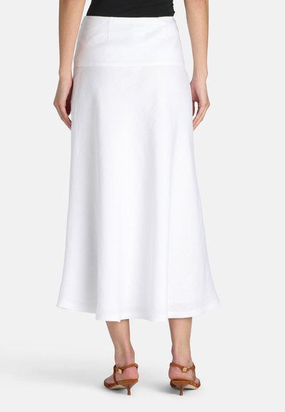 Kvinde iført hvid midi-længde A-formet nederdel og brune sandaler med lave hæle, vist bagfra mod en ensfarvet baggrund.