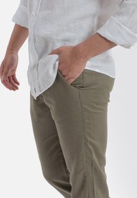 Biała lniana koszula z guzikami w połączeniu z oliwkowymi spodniami, cechującymi się gładką fakturą i bocznymi kieszeniami, dopasowanymi w talii i udach.