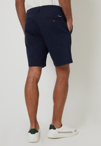 Shorts bleu marine au design classique, en coton. Dotés de deux poches arrière avec boutons et d'une texture unie. Associés à des baskets blanches.