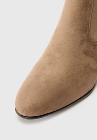 Bottines en suede beige avec un bout pointu et une texture lisse, dotées d'une semelle résistante et de détails de couture subtils le long des bords.