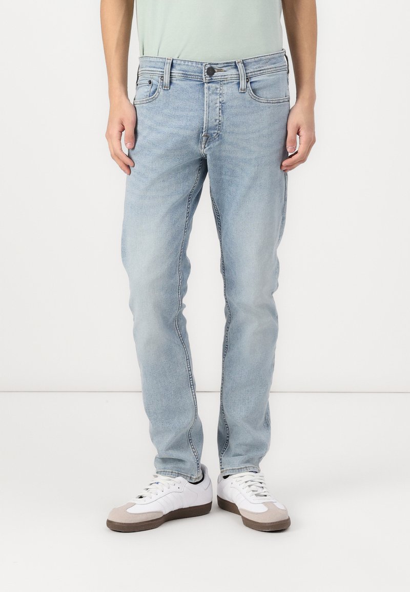 Jean en denim bleu clair avec une coupe droite, un design à cinq poches et un léger délavage. Associés à des baskets blanches avec des accents gris.