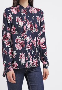Floral shirt made of soft, dark navy fabric, featuring pink and white flowers, a button-up front, and long sleeves with gathered cuffs.