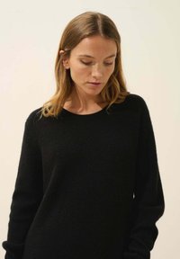 Černý pletený svetr s kulatým výstřihem a dlouhými rukávy. Tkanina vypadá měkce a texturovaně a má volný střih.