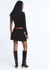 Fekete, hosszú ujjú felső, testhez simuló szabással és enyhe csillogással. Hozzáillő, fodros, ráncolt fekete szoknya, széles szegéllyel. Térdig érő fekete csizmák.