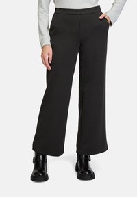 Schwarz karierte weite Hosen mit glatter Textur, ausgestattet mit zwei Seitentaschen und einem flachen Bund. Kombiniert mit schwarzen Ankle Boots.