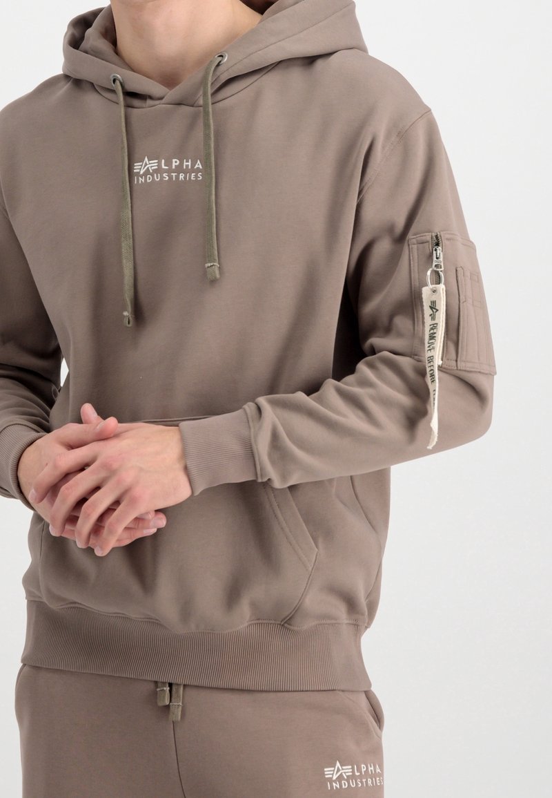 Sweat à capuche en tissu taupe, avec une poche avant, des poignets côtelés et un logo brodé sur la poitrine. Détail d'une poche zippée sur la manche.