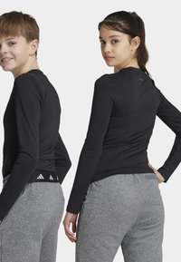 Zwarte sporttops met lange mouwen, een strakke pasvorm en een hoge nek, gecombineerd met grijze, gestructureerde sweatpants met een logoaccent op de tailleband.