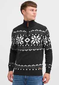 Strikket mørk grå genser med hvit snøflakmønster, høy krage, kvart glidelås, ribbede mansjetter og midje; har en liten brun logomerke.
