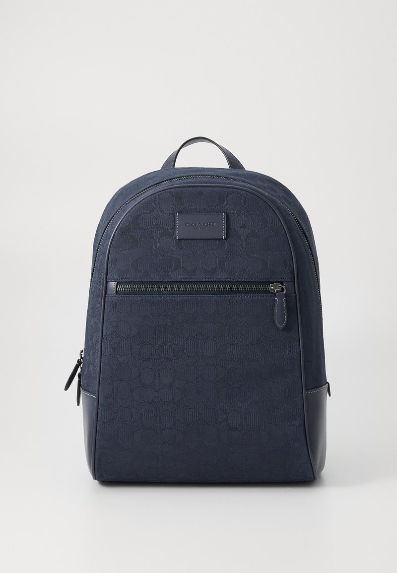 Navy blue backpack made of textured fabric with a smooth leather base. Features a front zipper pocket and a coach logo patch.