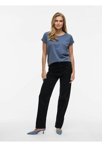 Grå t-shirt med kort ärm, svarta raka byxor och blåa mocka klackskor med spetsig tå, presenterade mot en neutral bakgrund.