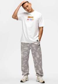 Camiseta blanca de algodón con un gráfico colorido de "PAC-MAN", combinada con pantalones joggers gris tie-dye y zapatillas beige con detalles en blanco y negro.