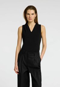 Black sleeveless top with a V-neck and subtle pleat details, paired with high-waisted, tailored black pants featuring a smooth finish.