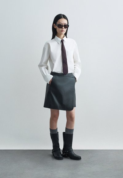 Λευκό πουκάμισο με μακριά μανίκια, σκούρη γραβάτα με πουά, γκρι δερμάτινη φούστα, μαύρες μπότες μέχρι το γόνατο με λουριά, και γκρι πλεκτές κάλτσες.