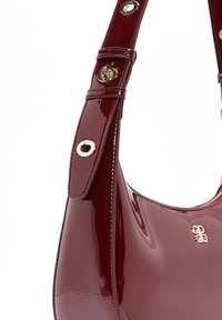 Bordeaux lakleren handtas met een gebogen vorm, voorzien van een gouden accent op de band en een logo vlak boven de opening.