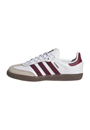 Sneaker bianca Adidas Samba con suola marrone, puntale in suede beige e tre strisce rosso scuro e linguetta sul tallone.