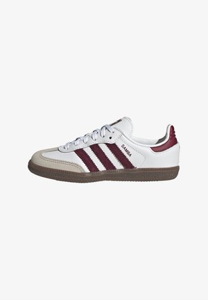 Λευκό αθλητικό παπούτσι Adidas Samba με καφέ σόλα, μπεζ καστόρινη μύτη και τρεις σκούρες κόκκινες ρίγες και ταμπέλα στη φτέρνα.