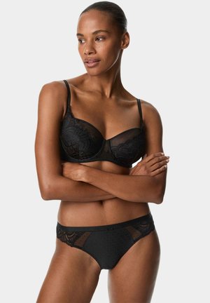 Schwarzes Dessous-Set bestehend aus einem Balconette-BH mit Spitzenverzierungen und durchsichtigem Mesh, kombiniert mit passenden schwarzen Panties mit Punkten und Spitzenakzenten.