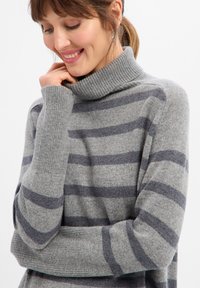 Szary sweter z golfem wykonany z dzianiny, z ciemnoszarymi poziomymi paskami, wyposażony w prążkowane mankiety i kołnierz. Miękka faktura, luźny fason.