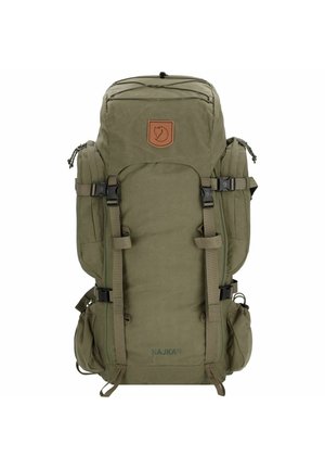 Mochila de tela verde con forma cuadrada, múltiples correas, bolsillos en los laterales, parche de logo marrón y cierre superior de cordón.