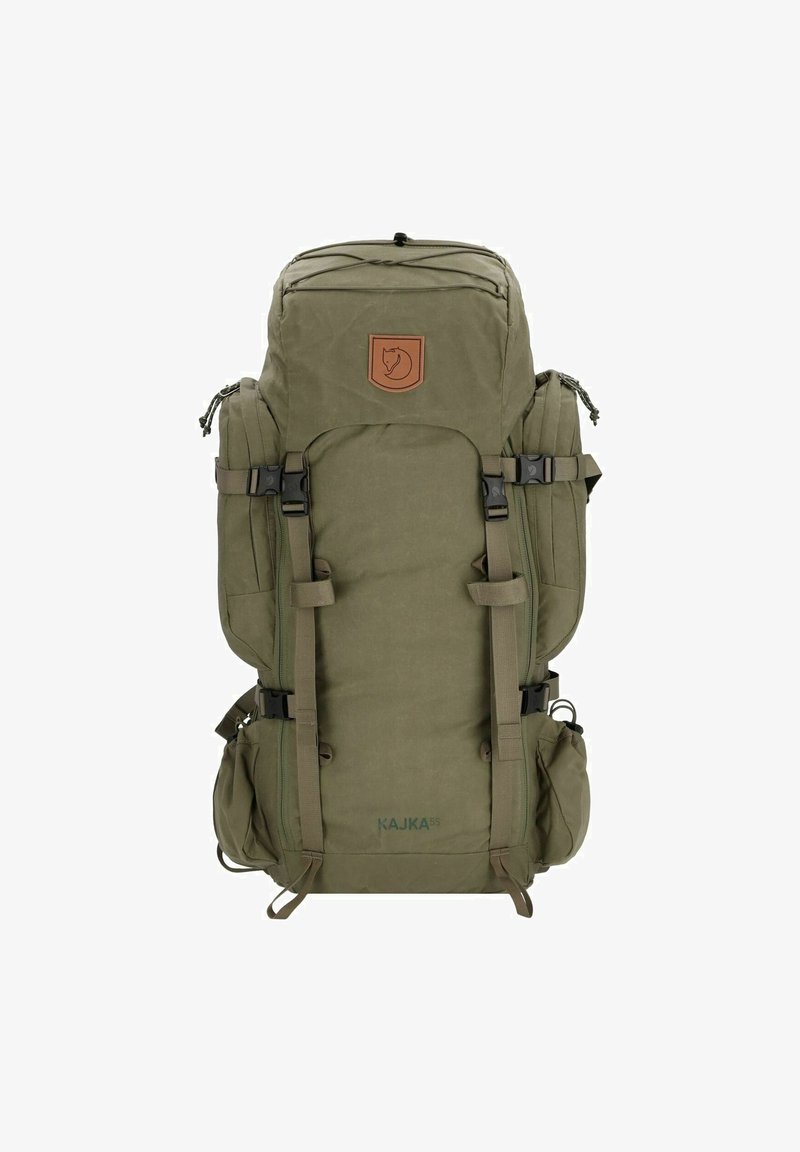 Žalias audinio kuprinė kvadrato formos, su keliomis diržais, šoninėmis kišenėmis, rudu logotipo pleistru ir viršutiniu uždarymu su raišteliu.