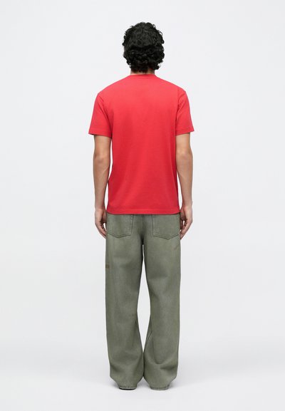 Punane puuvillane t-särk, lühikeste varrukatega, ümara kaelusega, sobitatud helesiniste laia säärega teksadega, millel on tagataskud ja minimaalne õmbluste detail.