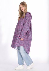 Abrigo impermeable púrpura de gran tamaño con estampado de leopardo rosa, con capucha, mangas largas y dobladillo recto. Combinado con vaqueros azul claro y zapatillas blancas.